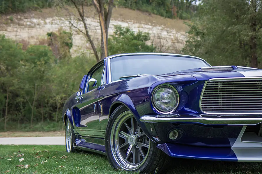 A restored purple Ford Mustang fastback parked on grass