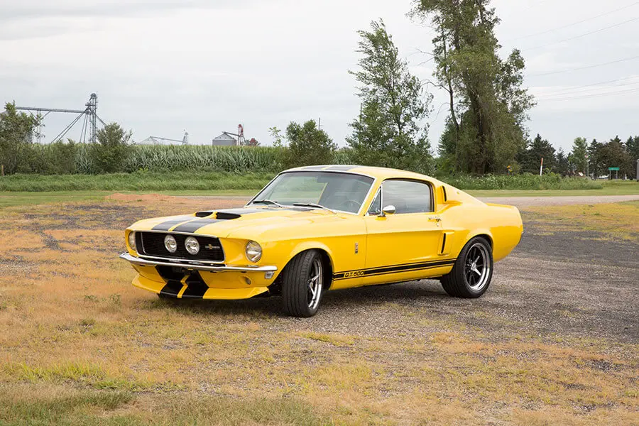 A yellow Shelby GT500 Mustang with black racing stripes parked on gravel